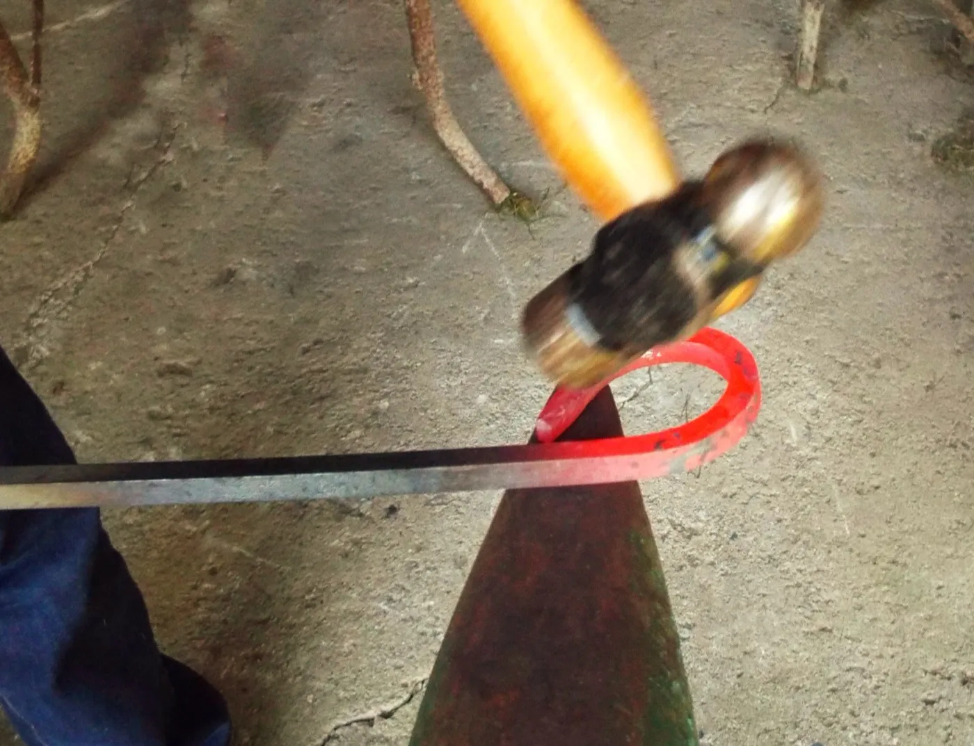 A blacksmith hammers a glowing, curved piece of iron on an anvil.